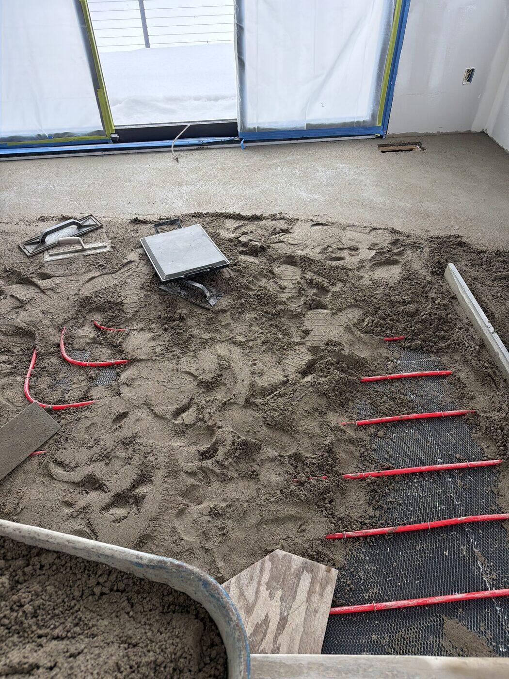 Mortar going down over red radiant heating tube and wire lath, hand float resting on the bed.