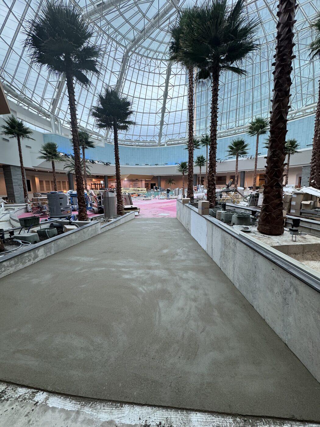 A floated walkway running between planters and mature palms beneath a glass atrium dome.