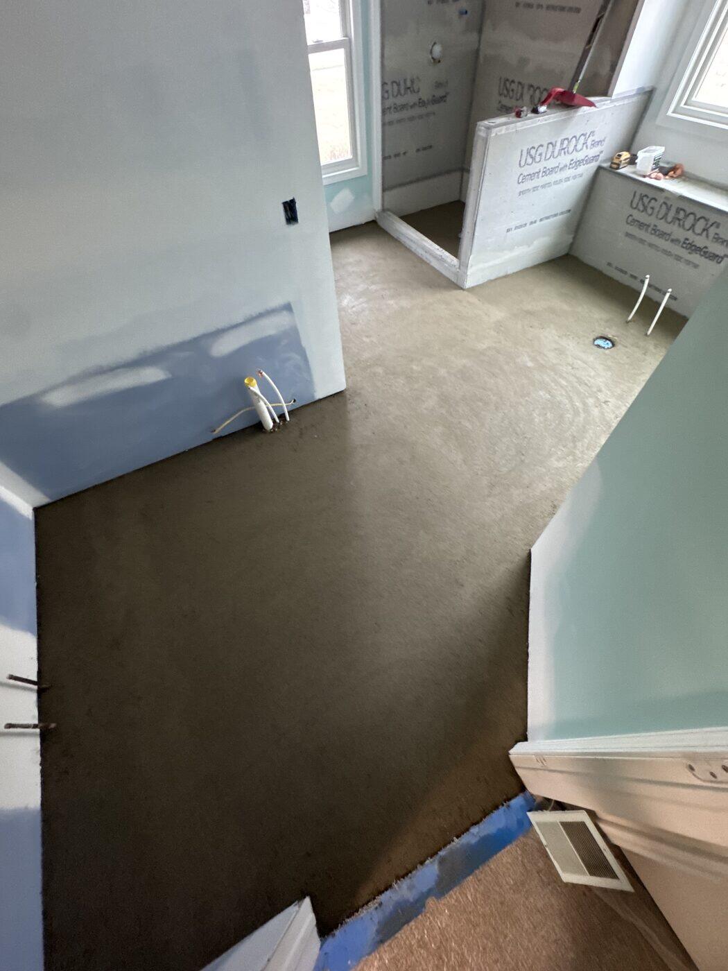A bathroom floor with the mortar bed poured, cement board on the walls and a shower alcove beyond.