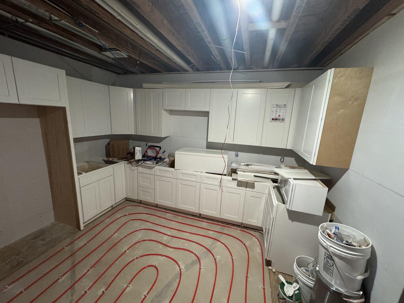 Red radiant heating loops stapled across a floor with kitchen cabinets already installed.